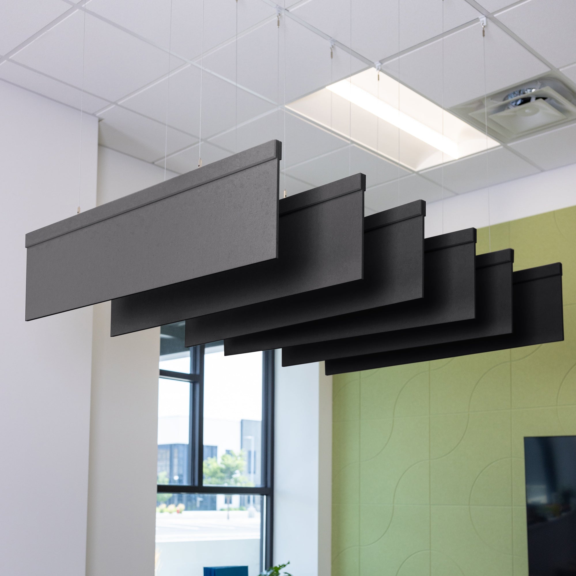 An interior office setting featuring a conference room with wooden tables and chairs, adorned with black acoustic blade baffles hanging from the ceiling.
