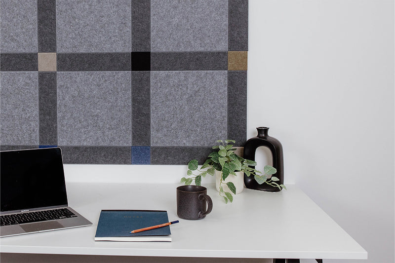 Pinnable Felt Right sound absorbing pinboard in a colorway that encourages focus. It has greys, blues, and neutrals. This pinboard is located behind a white desk with a computer on the desktop.