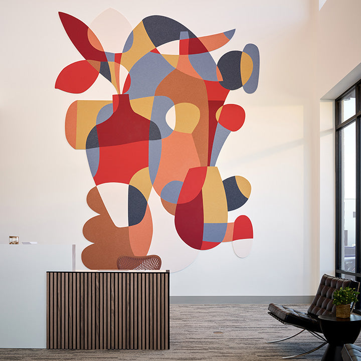A large abstract wall art piece with overlapping organic shapes in red, orange, yellow, blue, gray, and brown tones, displayed above a slatted wooden console in a modern interior room.