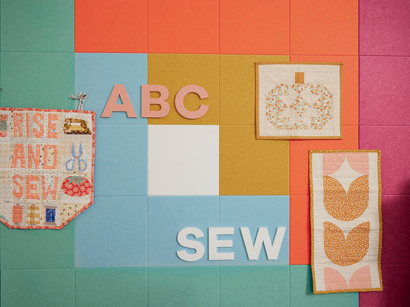 Colorful quilt with various sewing-themed blocks and text on a patchwork background.