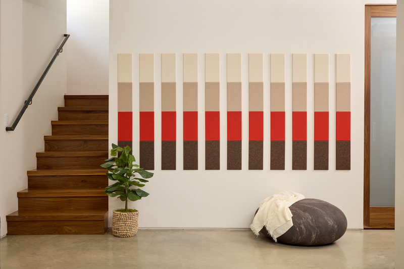 A Felt Right wall art design using browns, reds, and creams creating a pattern along a wall next to stairs and a house plant.