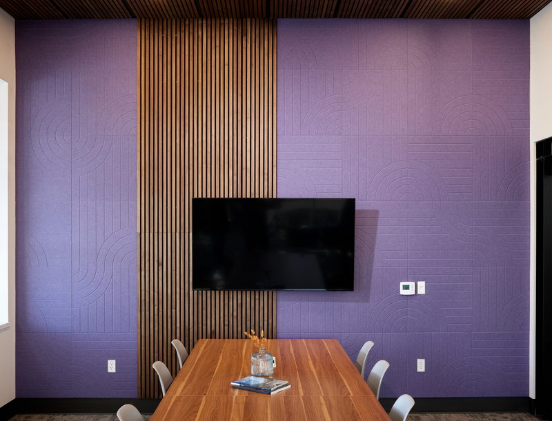 A Felt Right Wall design in a purple shade used in a conference room with a tv and wood in front of a conference table for an office or board room.