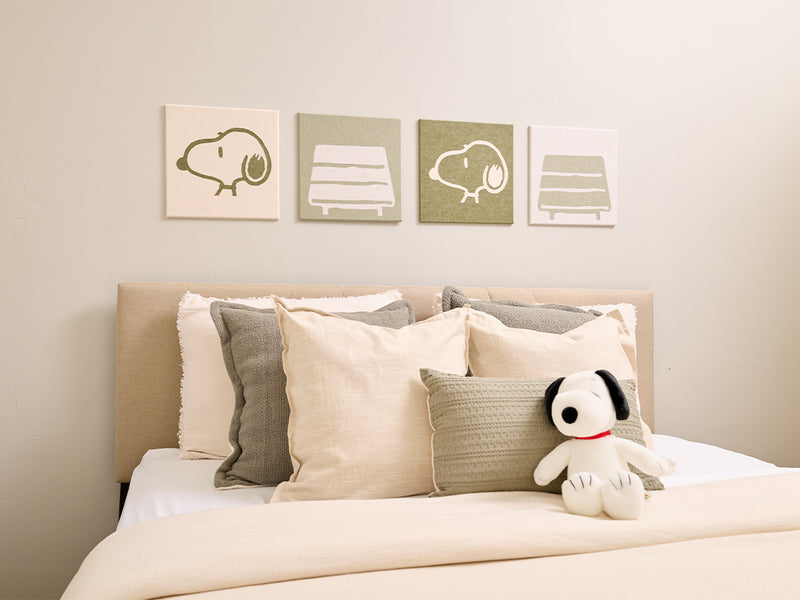 Bedroom with Snoopy plush toy and decorative pillows on a bed, featuring Snoopy illustrations on the wall.
