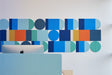 A Felt Right wall art design in shades of blue, orange, and yellow creating a geometric wall art pattern behind a desk and a computer