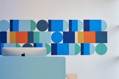 A Felt Right wall art design in shades of blue, orange, and yellow creating a geometric wall art pattern behind a desk and a computer