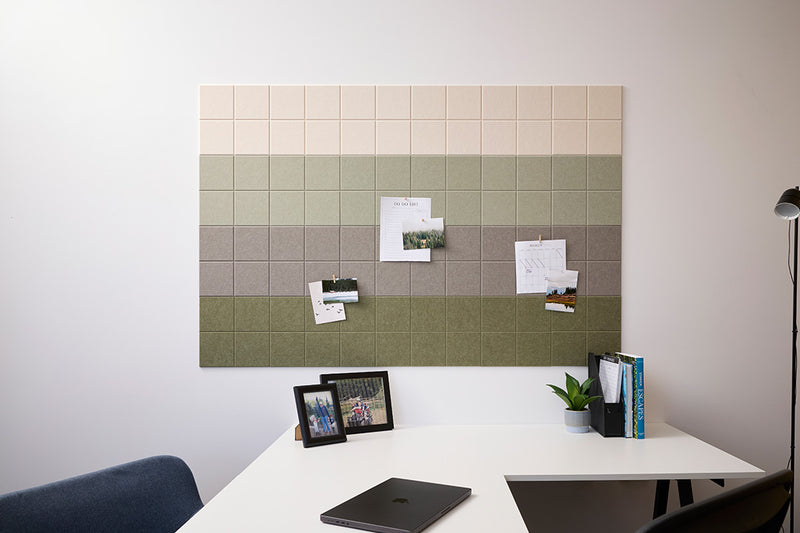 A Felt Right wall design that can work as a bulletin board with a green ombre design, mounted on a wall above a white desk. The board is decorated with notes, photos, and pins.