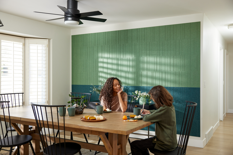 A Felt Right wall design in green and blue used in a dinning room next to a dinning table with two people eating.