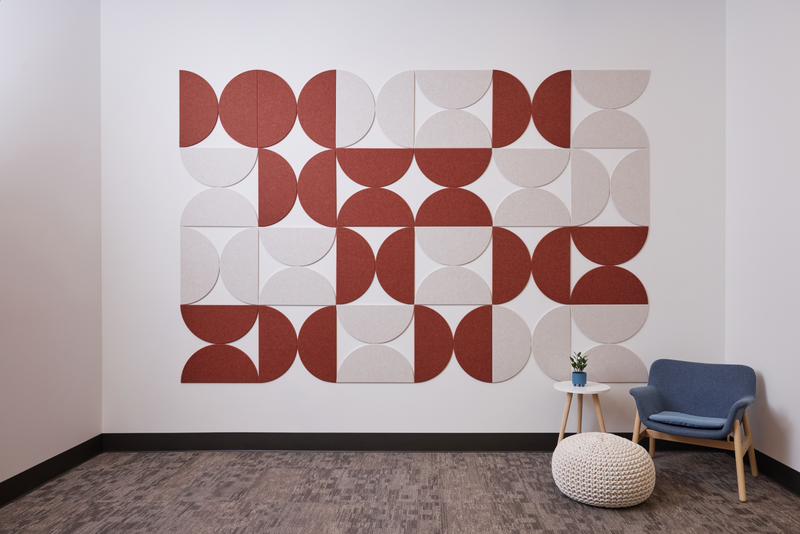 A Felt Right wall art design in shades of red and cream half circle tiles on a white wall with a chair and small side table.