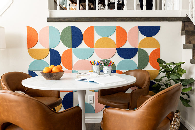 Felt Right wall art design using half circles in orange, yellow, blue, green, pink on a wall next to a table and four chairs