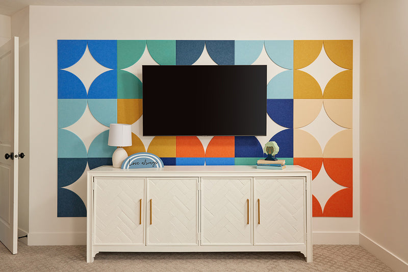 A Felt Right wall art design using quarter circles in shades of blue, orange, yellow, and cream to make  a back drop behind a tv and a tv stand.