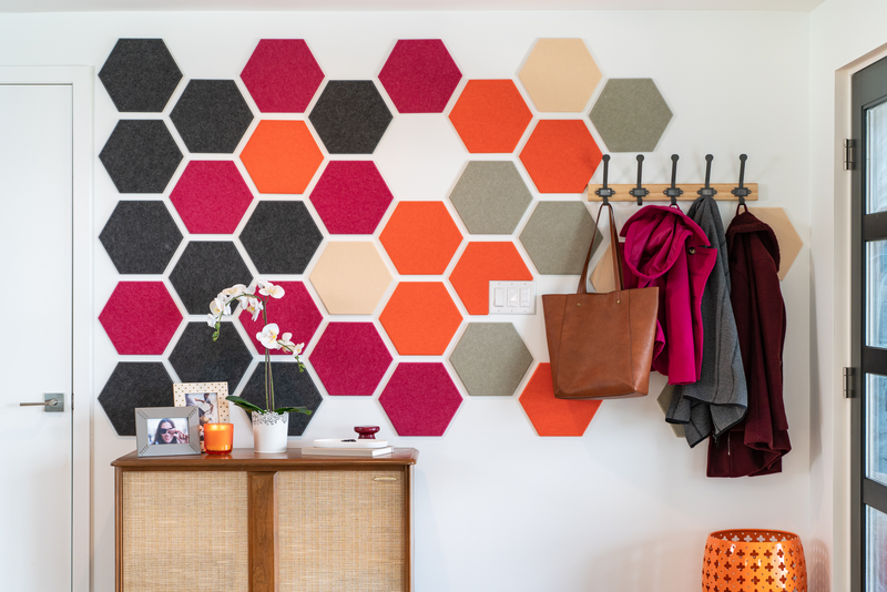 A Felt Right wall art design using hexagons to create a geometric pattern in grey, pink, cream, and orange next to door and a coat rack