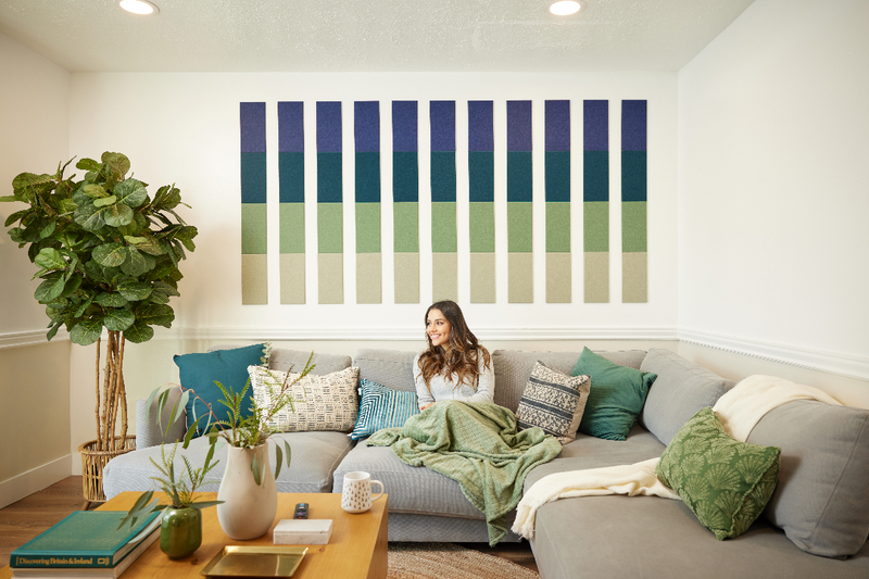A Felt Right Wall Design in blues, greens, and creams set above a couch in a living room with a tree and a coffee table