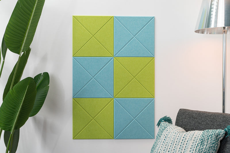 A Felt Right wall design made of felt and used as bulletin board with checkered shaped frames in blue and green shades, mounted on a wall next to a lamp and a plant.