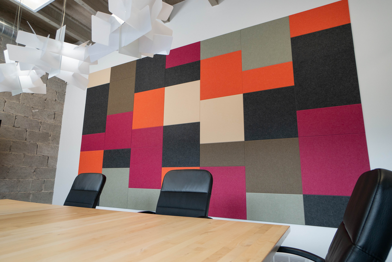 A Felt Right wall art design in shades of pink, brown, black, green, orange, and cream felt tiles on a white wall in a conference room or office.