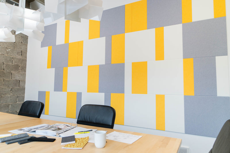 A Felt Right wall art design in shades of white yellow and grey felt tiles on a white wall in a conference room.