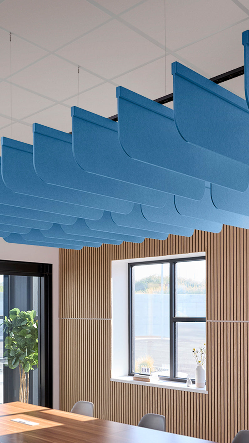 Bright blue acoustic ceiling blade baffles suspended from the ceiling, installed in a conference room. Felt Right's acoustic blade baffles absorb 65% of sound waves, making office spaces quieter and feel more calm.