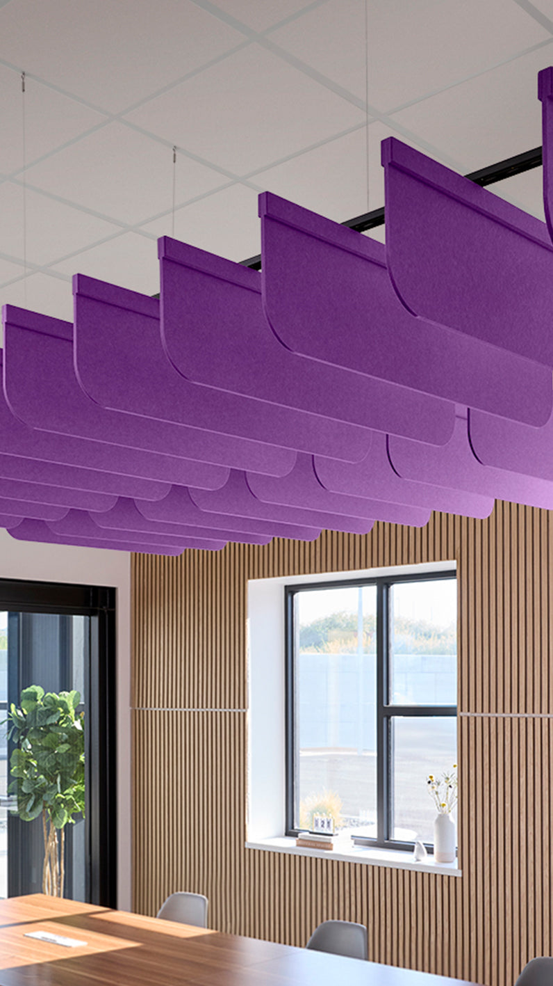 Purple acoustic ceiling blade baffles suspended from the ceiling, installed in a conference room. Felt Right's acoustic blade baffles absorb 65% of sound waves, making office spaces quieter and feel more calm.