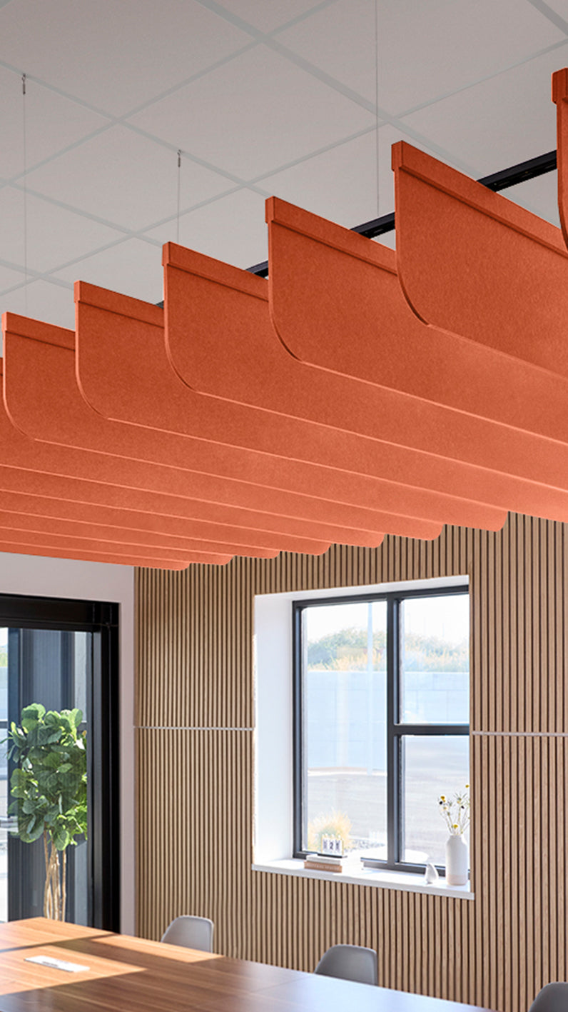 Orange acoustic ceiling blade baffles suspended from the ceiling, installed in a conference room. Felt Right's acoustic blade baffles absorb 65% of sound waves, making office spaces quieter and feel more calm.