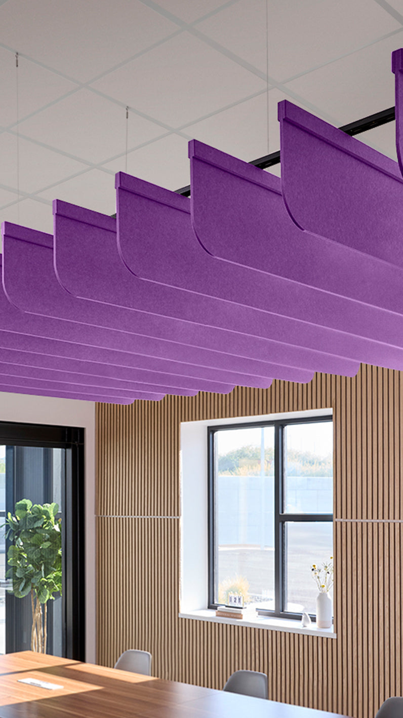 Purple acoustic ceiling blade baffles suspended from the ceiling, installed in a conference room. Felt Right's acoustic blade baffles absorb 65% of sound waves, making office spaces quieter and feel more calm.