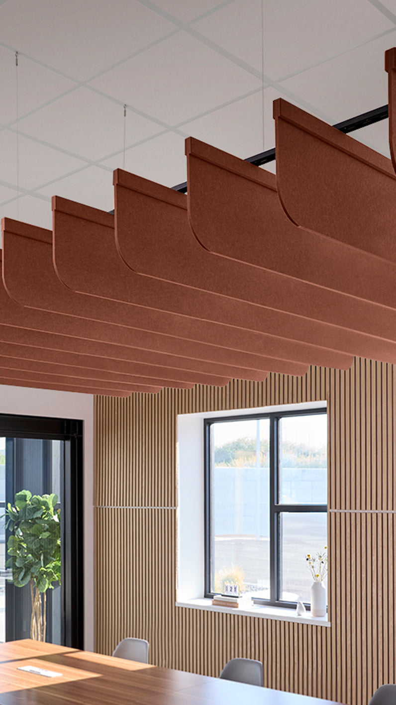 Reddish-brown acoustic ceiling blade baffles suspended from the ceiling, installed in a conference room. Felt Right's acoustic blade baffles absorb 65% of sound waves, making office spaces quieter and feel more calm.