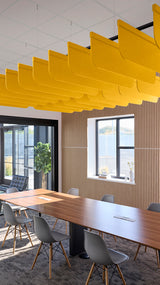 Yellow curved acoustic baffles suspended from ceiling in office space above conference table.