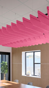 Multiple pink curved acoustic baffles suspended from ceiling in a row above wooden slat wall.