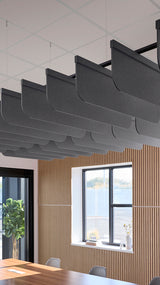 Dark gray curved acoustic baffles suspended from ceiling in office space with wooden wall paneling and windows.