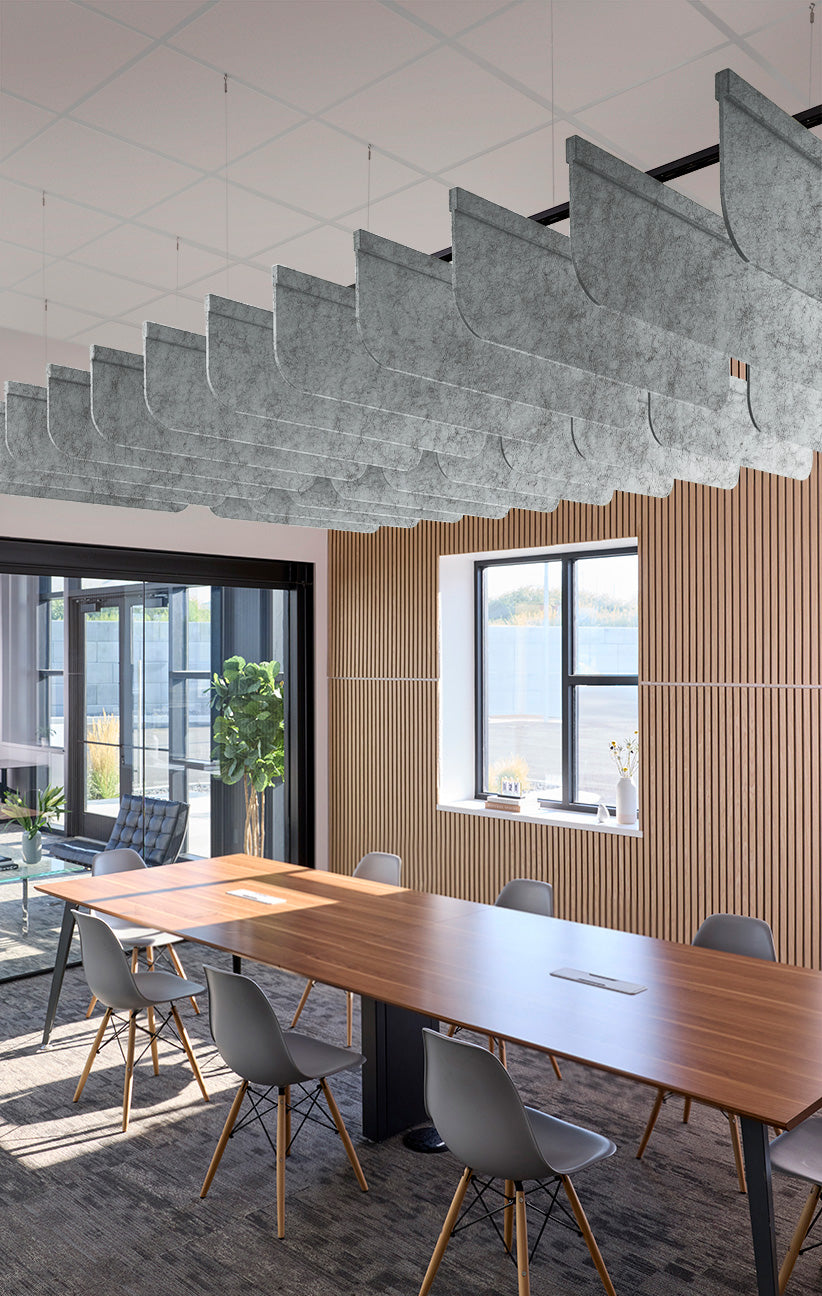 A modern conference room with a long wooden table, gray chairs, a slatted wood wall, and a large sculptural gray ceiling light fixture.