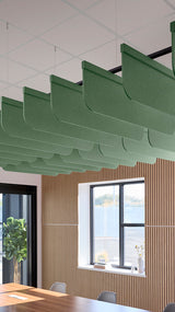 Multiple green curved acoustic baffles suspended from ceiling grid in office space with wood wall paneling and windows.