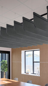 Dark gray acoustic baffles with curved edges suspended from ceiling grid above wooden wall paneling and windows.