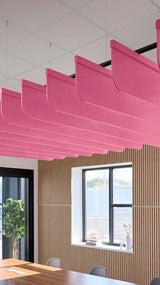 Pink fabric acoustic baffles suspended from ceiling above wooden wall paneling and windows in modern office space.