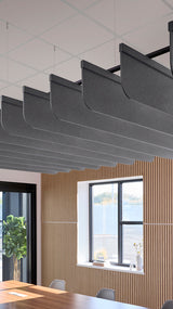 Row of curved dark gray acoustic baffles suspended from ceiling above wood-paneled wall with windows.
