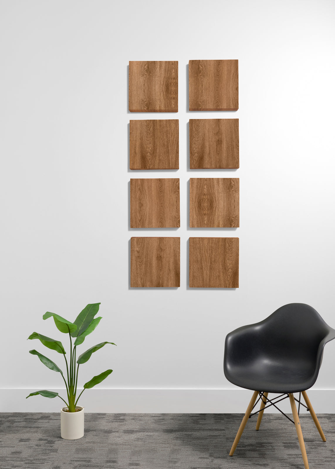 Eight square wooden wall panels with a natural wood grain finish are arranged in a grid on a white wall. The scene is styled with a black molded plastic chair with wooden legs on the right and a green potted plant on the left, set against a gray textured floor.