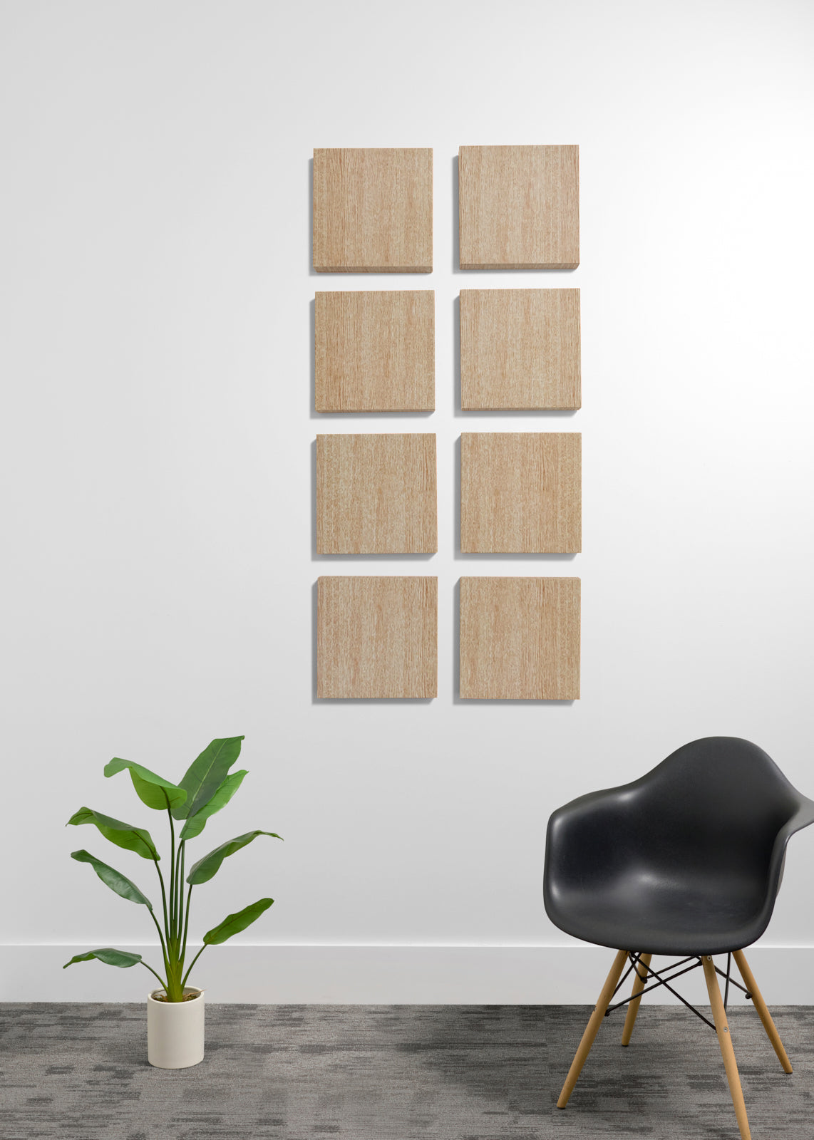 Eight square light wood panels arranged in two columns of four on a white wall in a modern room setting, with a potted green plant and a black molded chair on a gray floor.