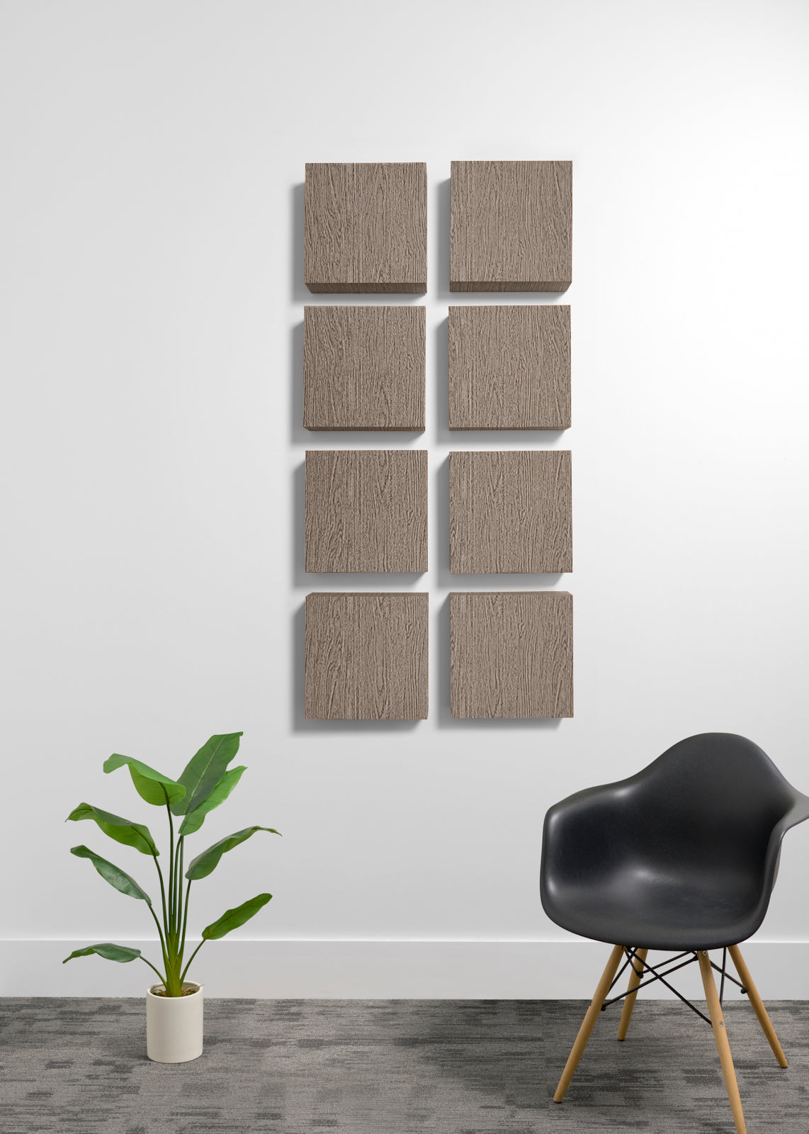 Eight square wall art panels with a light brown wood grain texture arranged in two vertical columns of four on a white wall, styled in a modern room with a black chair and a potted plant.