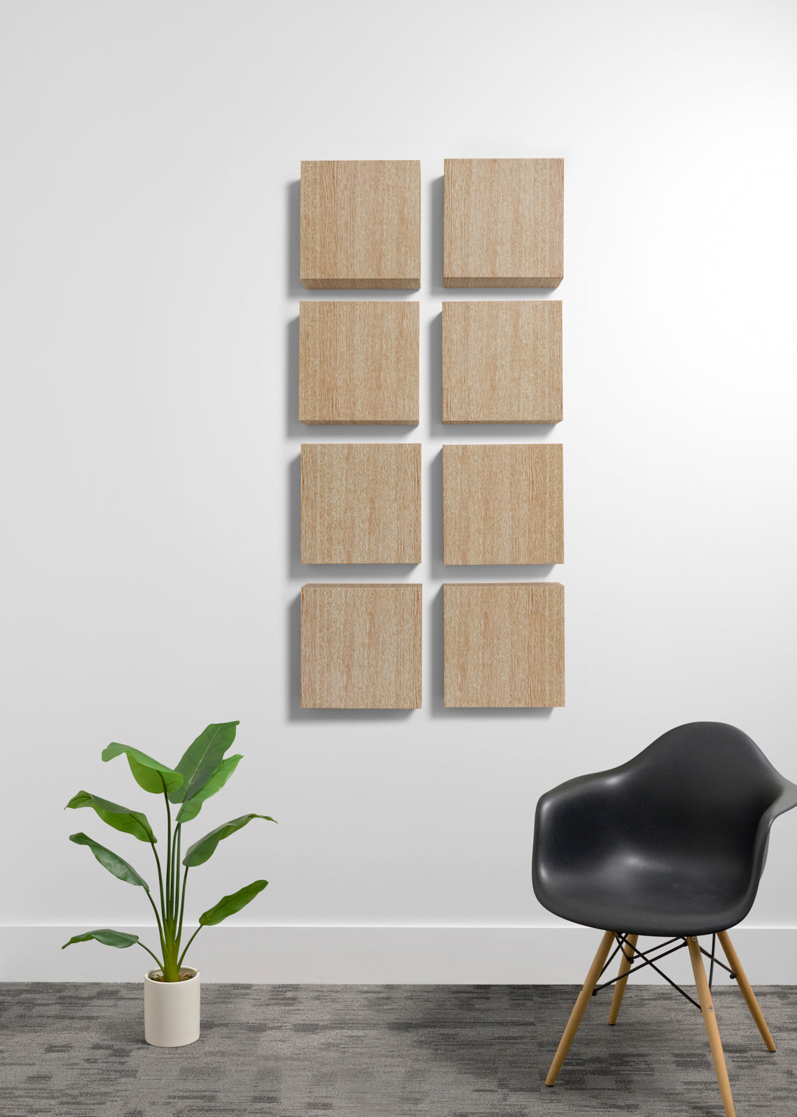 Eight square light wood wall panels arranged in two vertical columns of four on a white wall, shown in a styled room with a black chair and a potted plant.