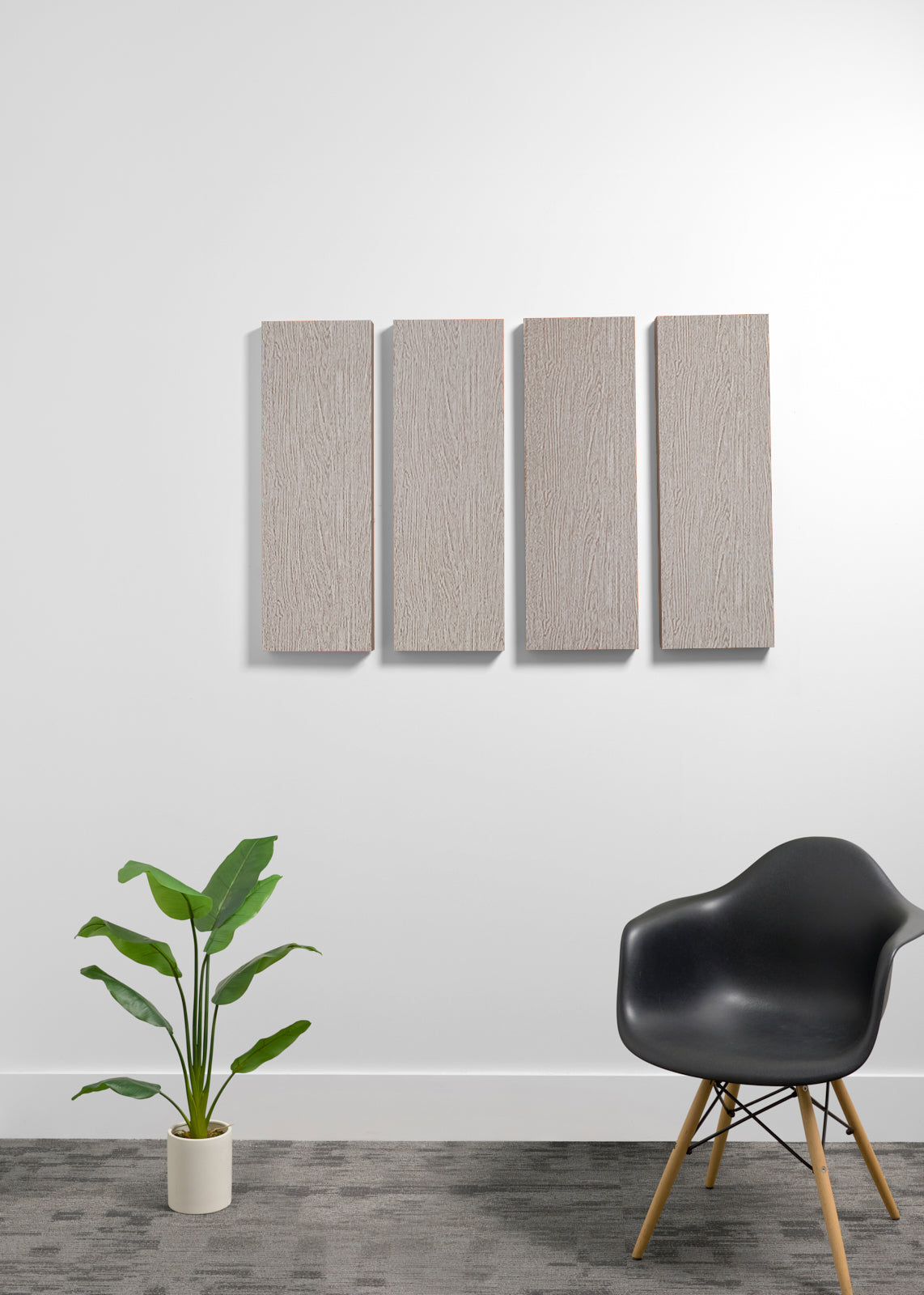 Four rectangular wall panels with a light wood grain finish mounted on a white wall, styled in a modern room setting with a black chair and a potted plant.