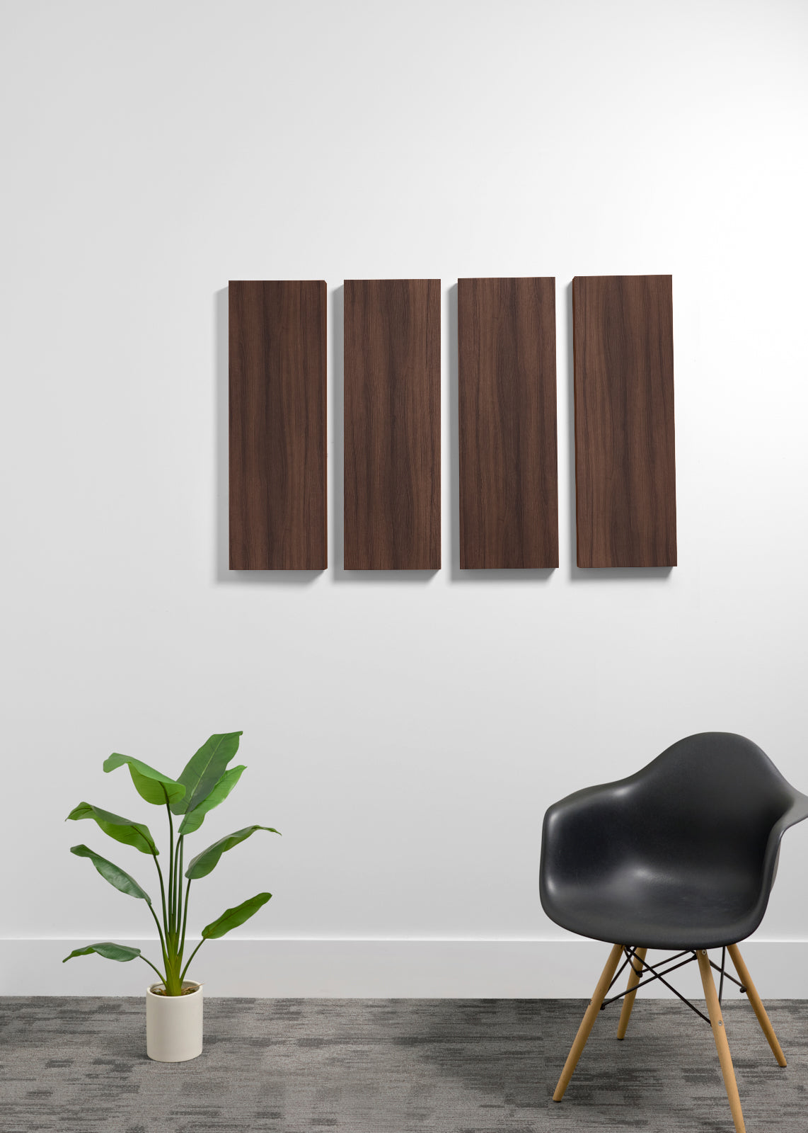Four vertical dark brown wood panels mounted on a white wall above a gray floor, with a potted green plant on the left and a black molded chair with wooden legs on the right.