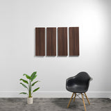 Four dark wood-finish rectangular acoustic panels mounted on white wall above black chair and potted plant.