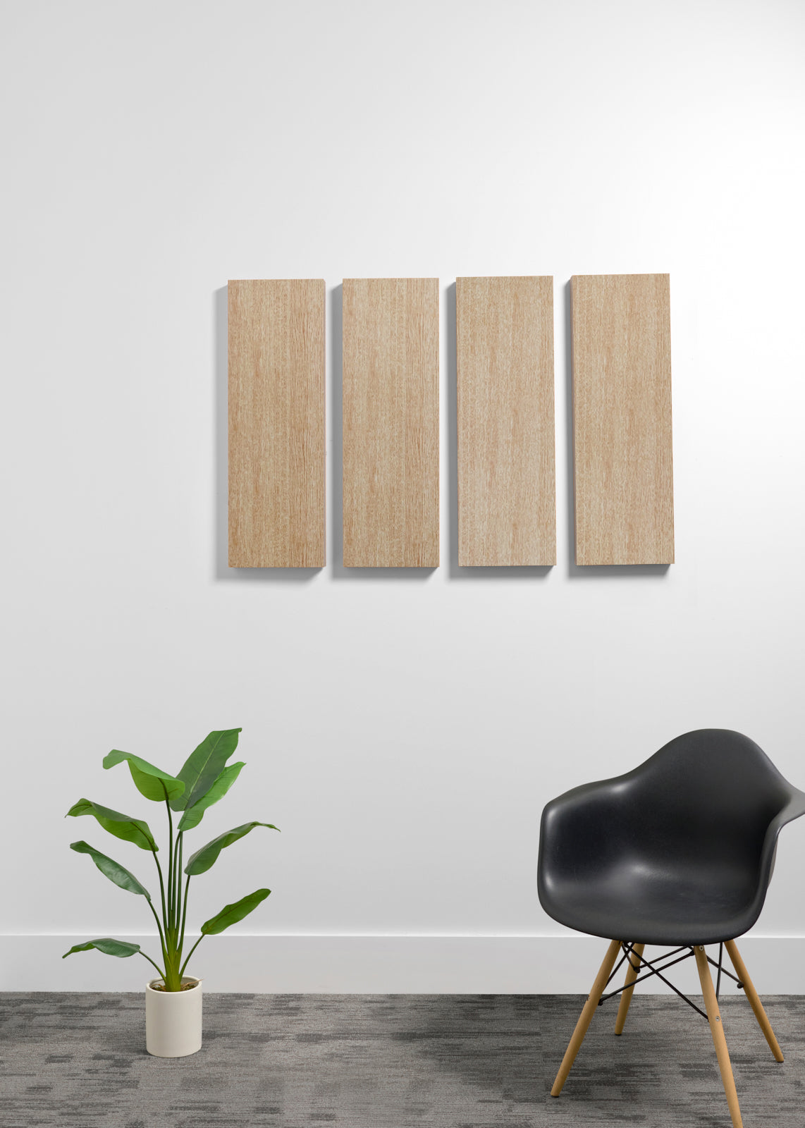 Two square light wood wall art panels hanging vertically on a white wall in a modern room setting, with a black chair and a potted green plant below.
