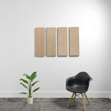 Four rectangular wooden acoustic panels mounted on white wall above chair and plant.