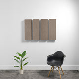 Set of four rectangular gray acoustic panels mounted on white wall above chair and plant.