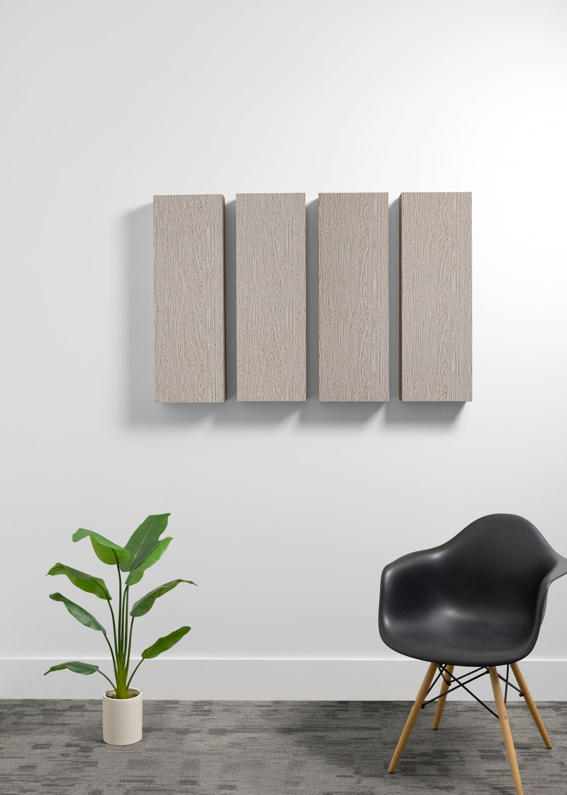 Four rectangular wall panels with a light wood grain finish mounted on a white wall, styled in a modern room setting with a black chair and a potted plant.