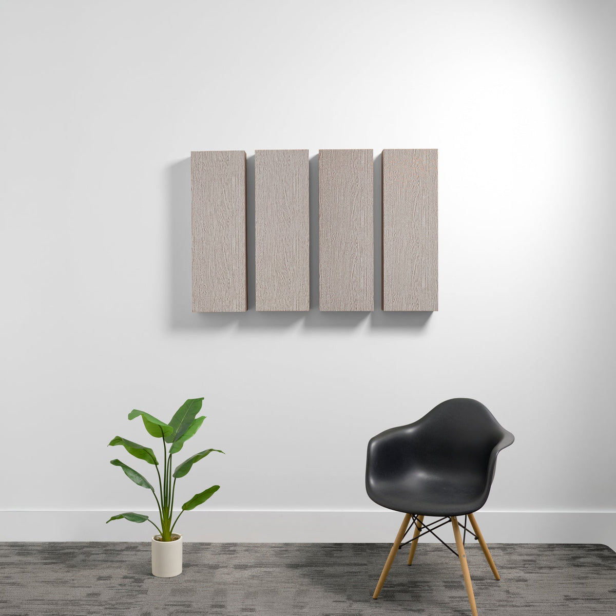Four rectangular beige acoustic panels mounted on white wall above black chair and potted plant.