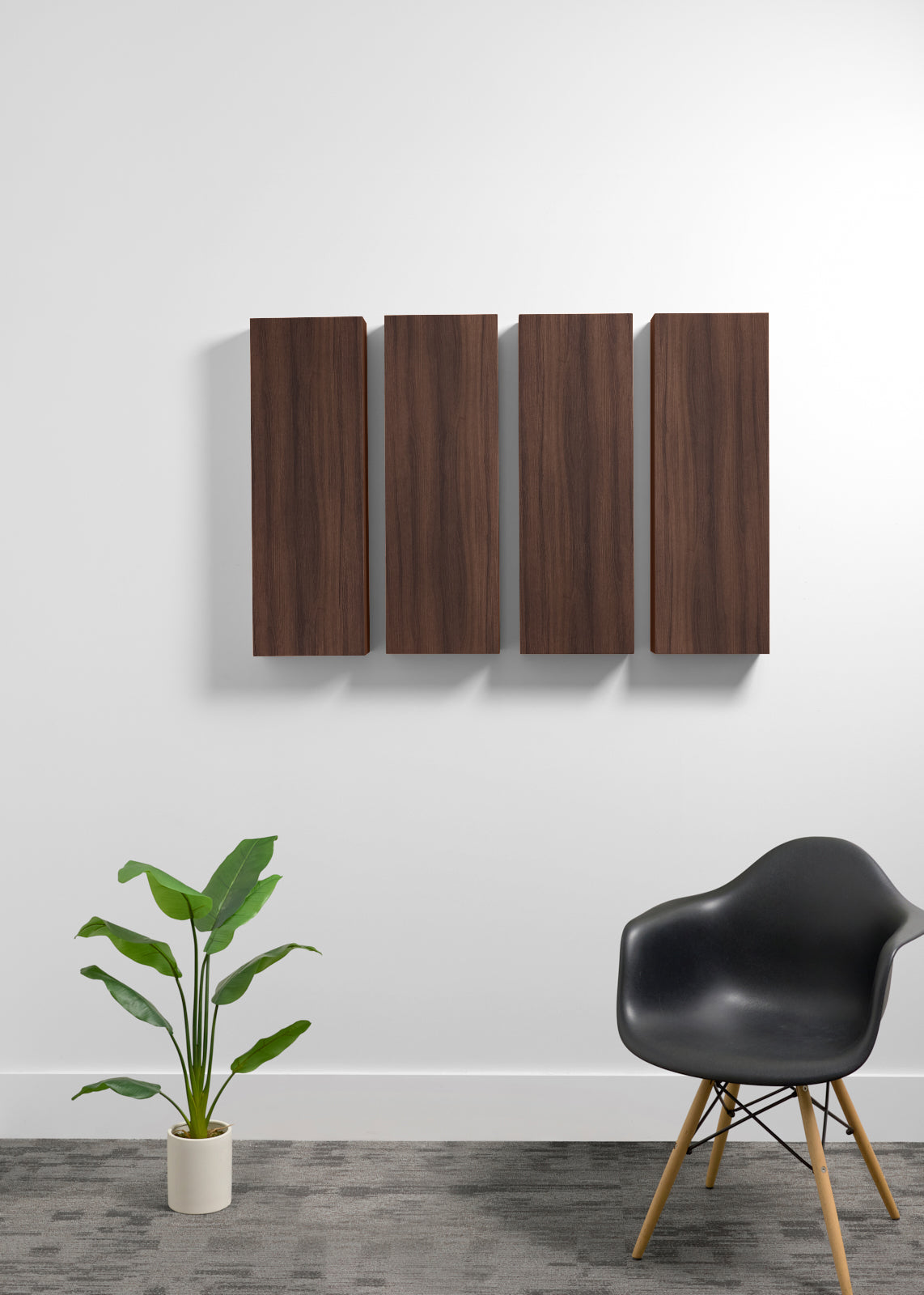Four vertical dark brown wood panels mounted on a white wall above a gray floor, with a potted green plant on the left and a black molded chair with wooden legs on the right.