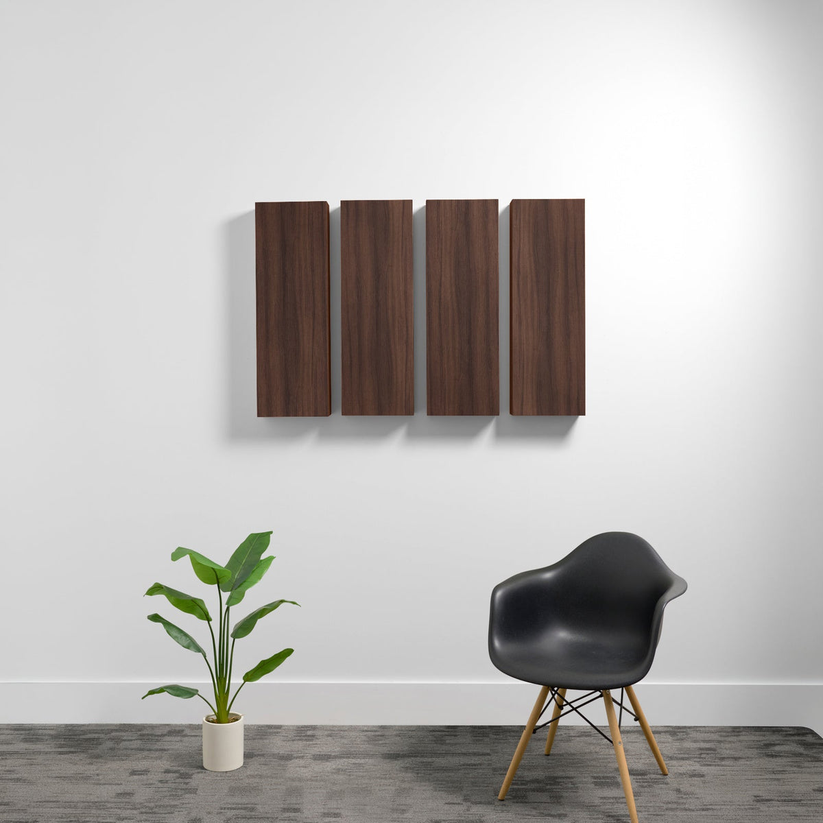 Four rectangular dark wood acoustic panels mounted on a white wall above a black chair and potted plant.