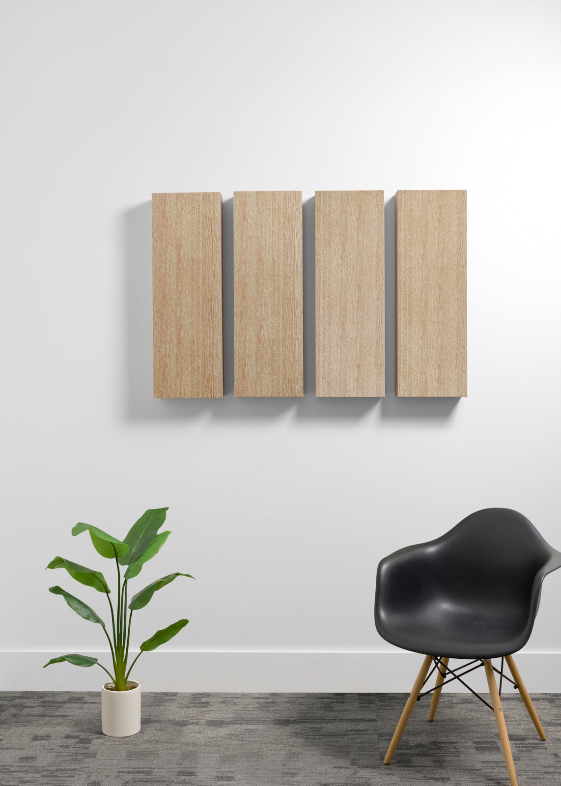 Two square light wood wall art panels hanging vertically on a white wall in a modern room setting, with a black chair and a potted green plant below.