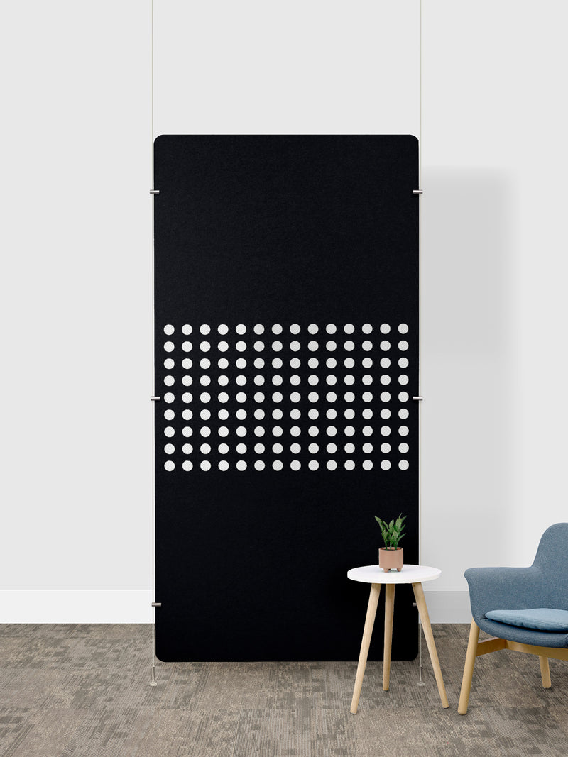 Black room divider panel with white perforated circular pattern, mounted on floor with metal anchoring hardware.