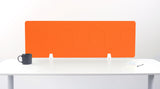Orange desk divider with curved wave pattern, mounted on white desk with black mug and notebook visible.