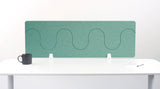 Teal desk divider with wavy pattern mounted on white desk with supports.